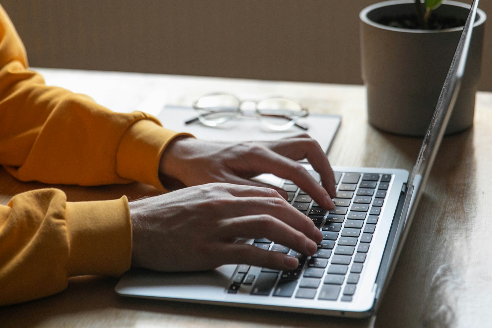 Hands typing on a laptop on a wooden table